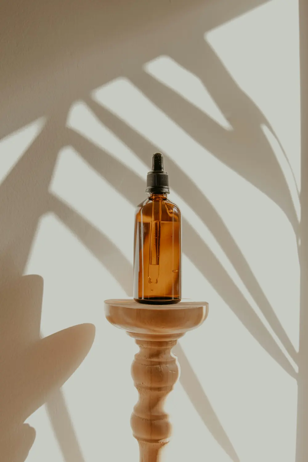 An amber dropper bottle on a turned wooden stand, with soft leaf shadows