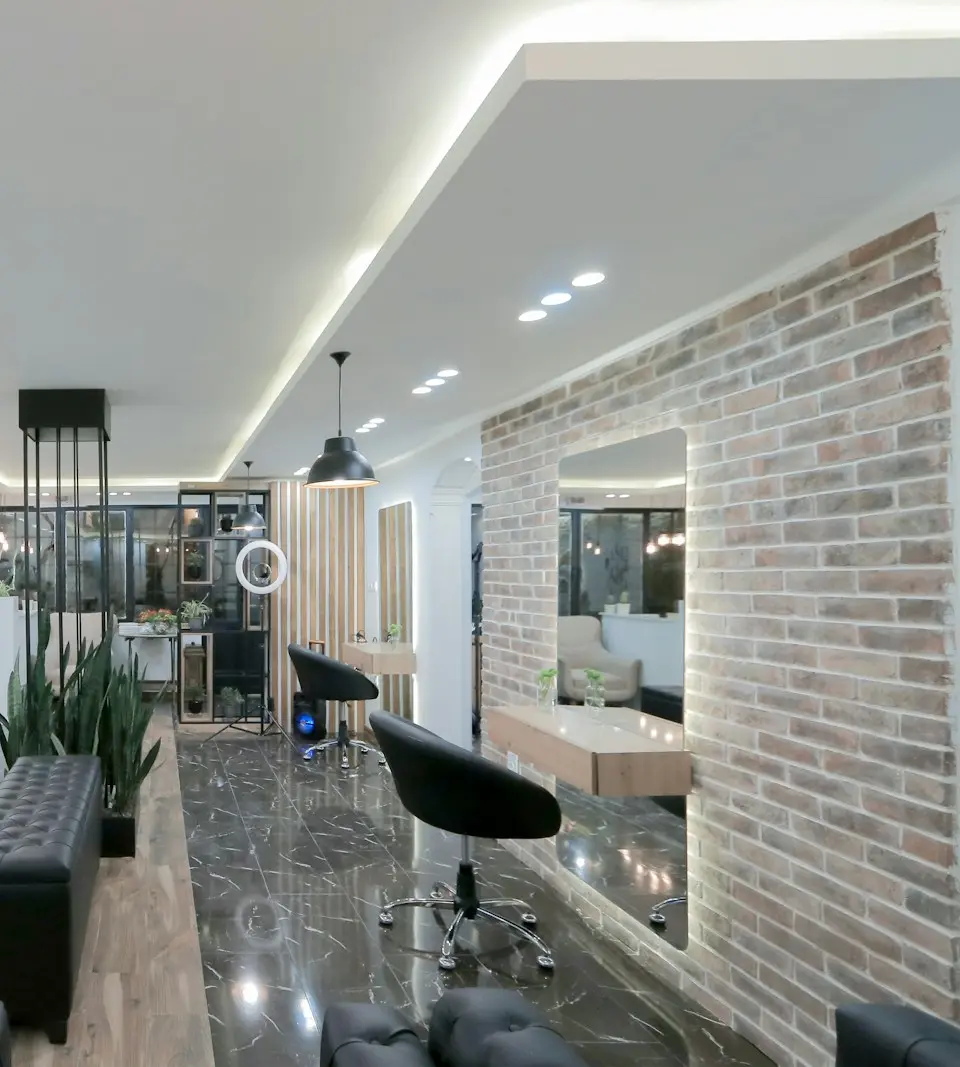 A bright salon with black styling chairs, a brick wall and a long mirror