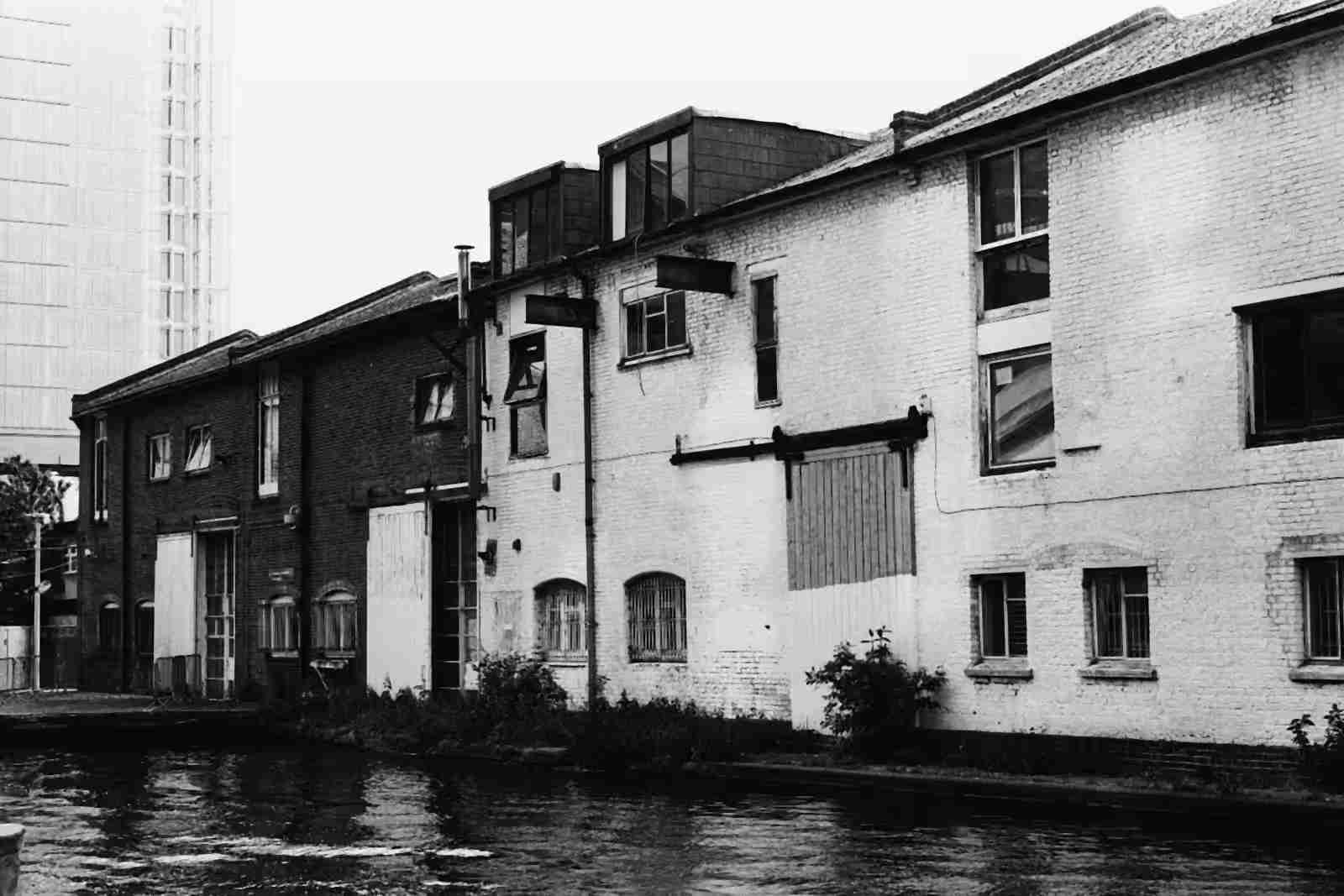 Old brick and whitewashed warehouses along a canal, in black and white.