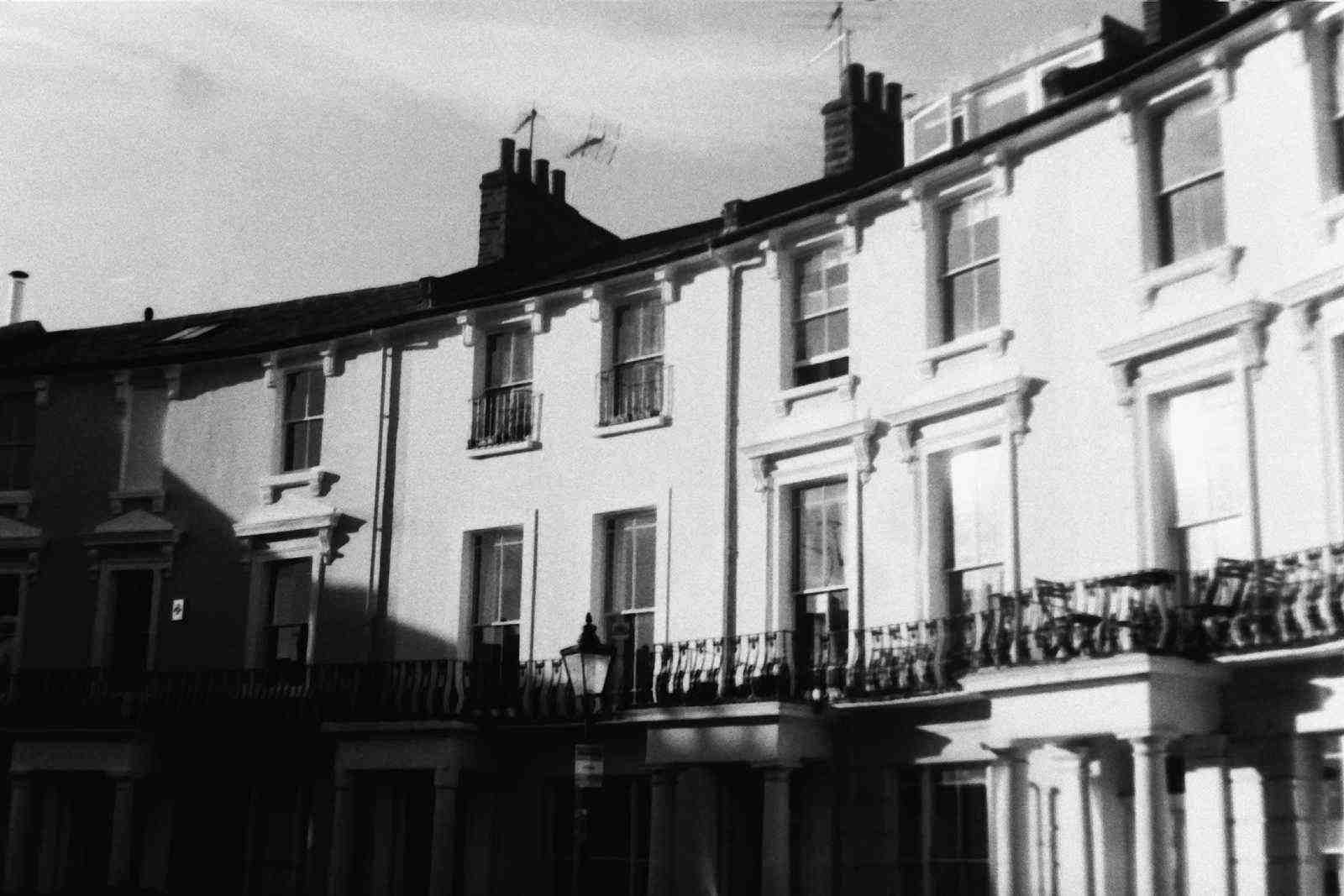 A curved terrace of white stucco houses with iron balconies, in hard sunlight.