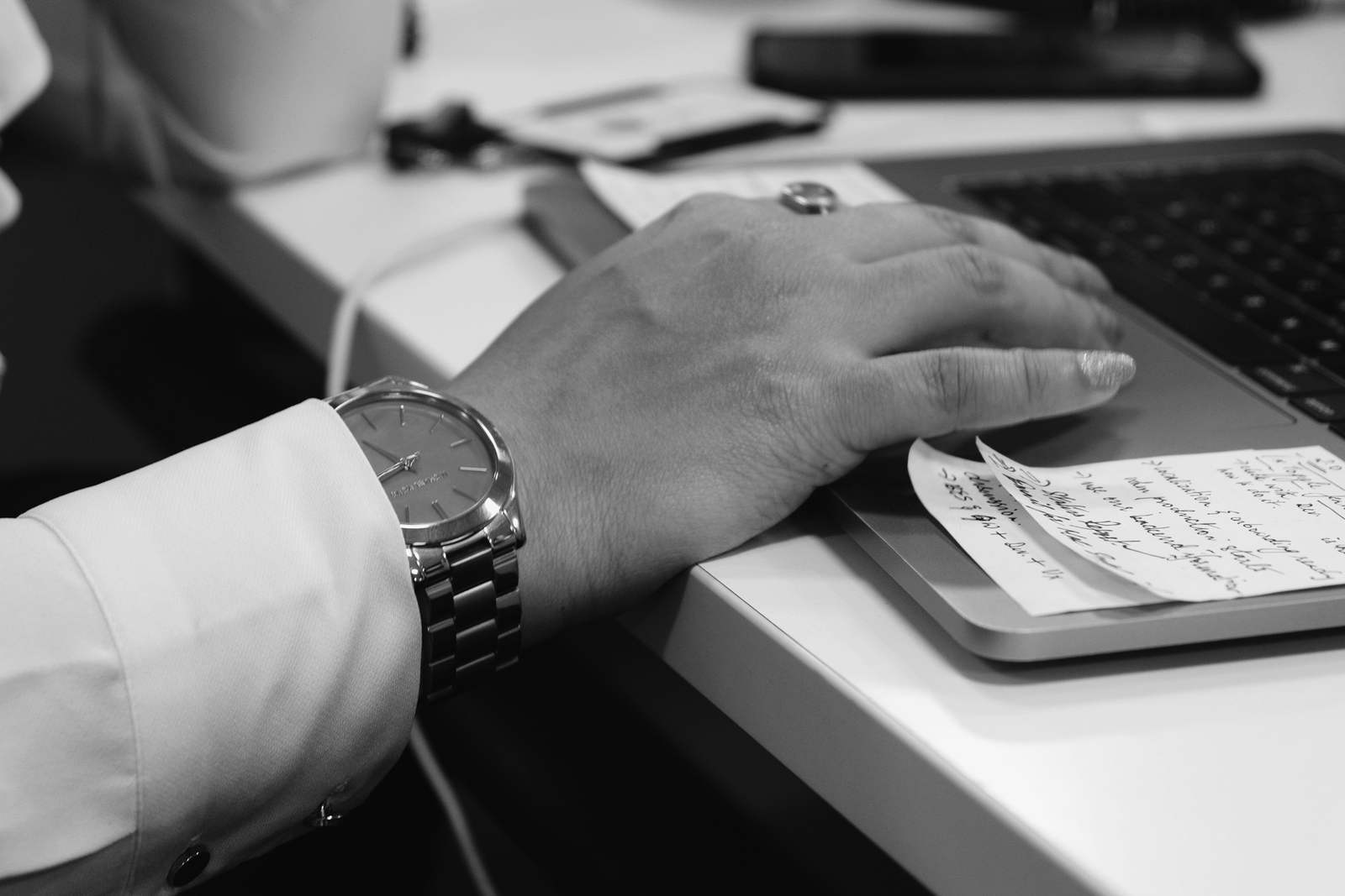 A hand on a laptop trackpad, with a handwritten note tucked beside the keyboard.