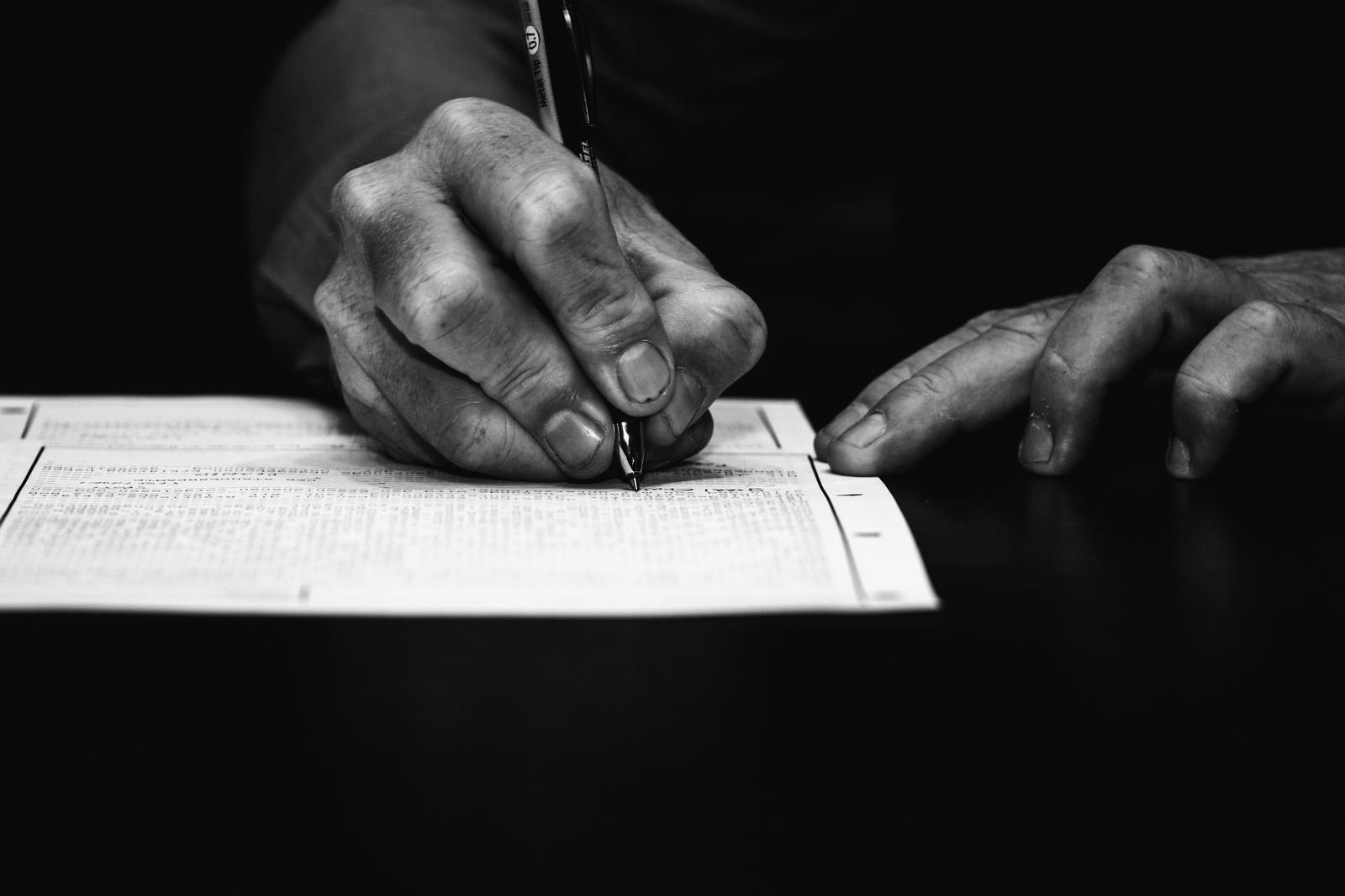 Close-up of a hand signing a printed form with a fountain pen, on a dark desk.