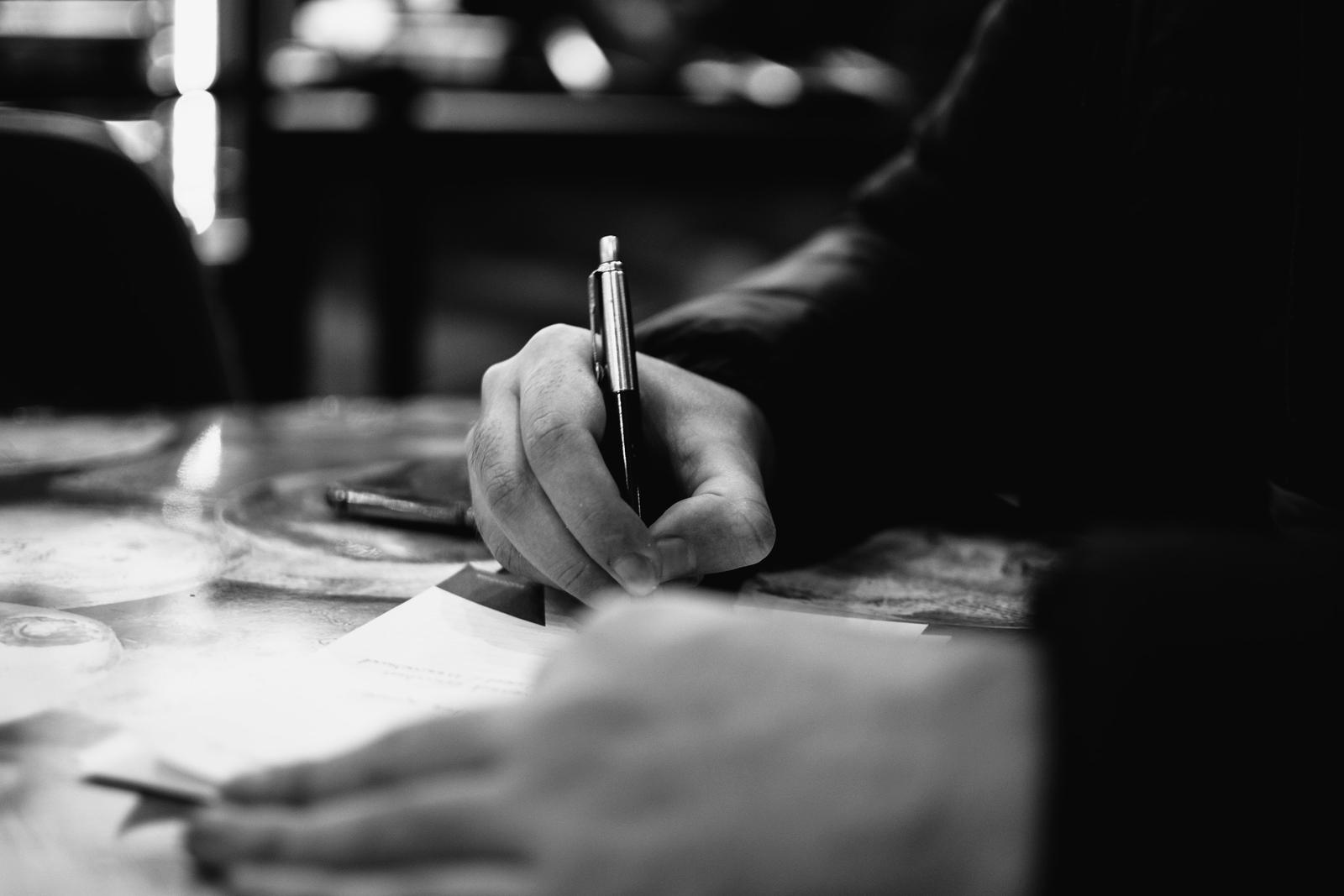 A hand filling in a printed form with a ballpoint pen.