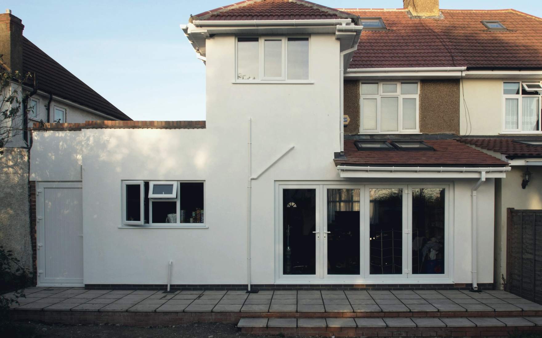 After: the finished single-storey rear extension in white render, with wide garden doors and rooflights, on a 1930s semi