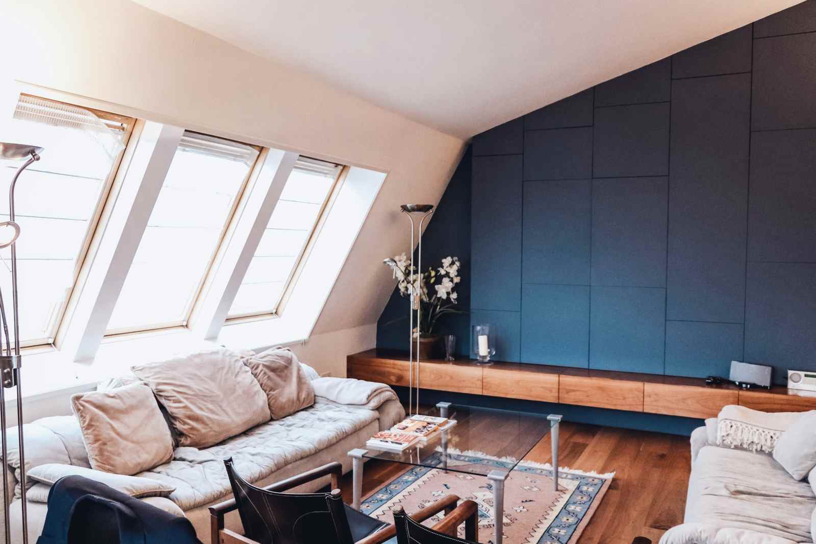 After: the finished loft room with a row of rooflights, a sofa and deep blue joinery