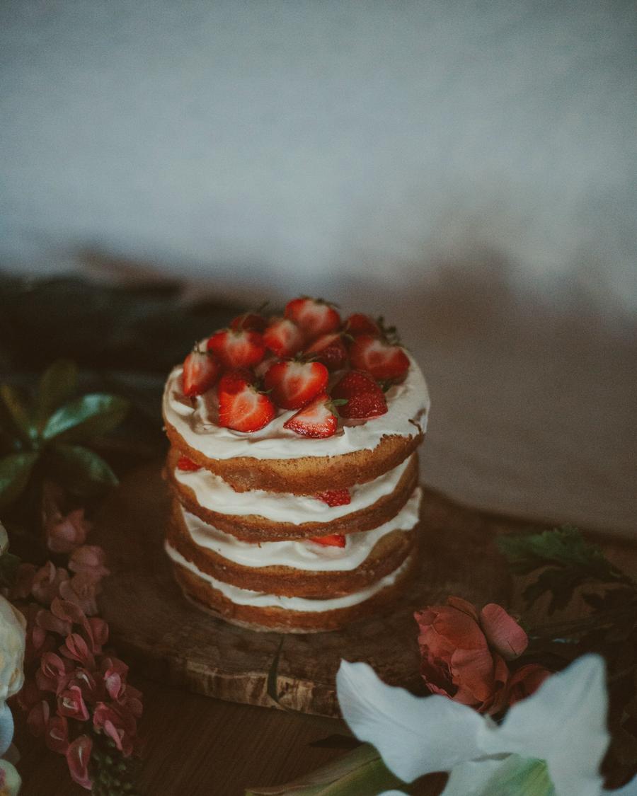 A tall semi-naked cake with berries in low light
