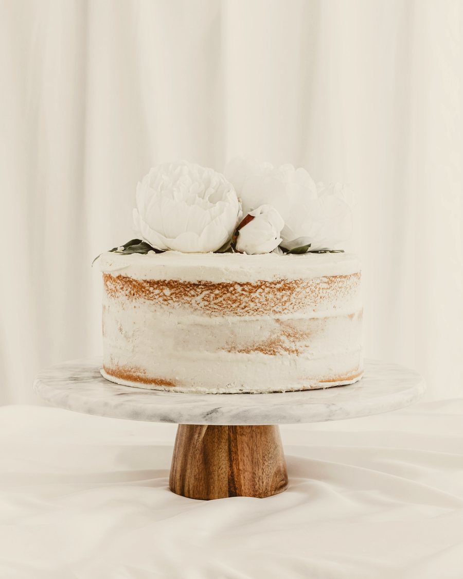 A semi-naked white sponge cake with fresh white flowers on a wooden stand