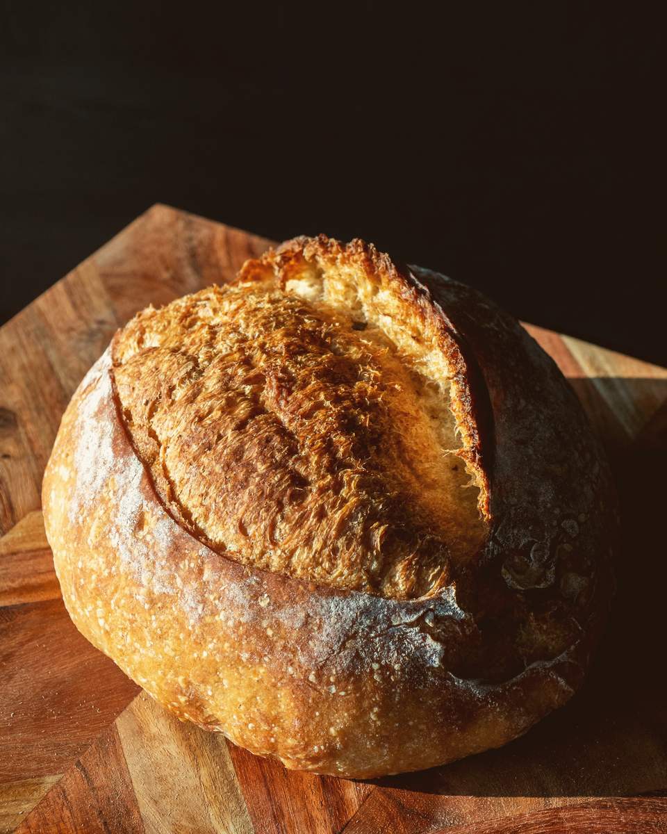 A dark-crusted sourdough loaf with a tall, open ear, resting on a wooden board