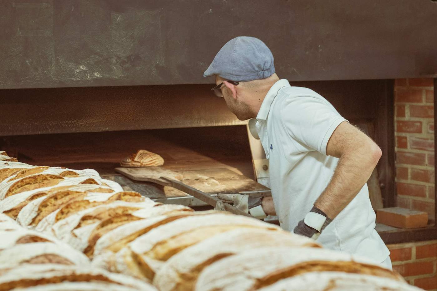 A baker loading scored loaves into a brick-lined deck oven