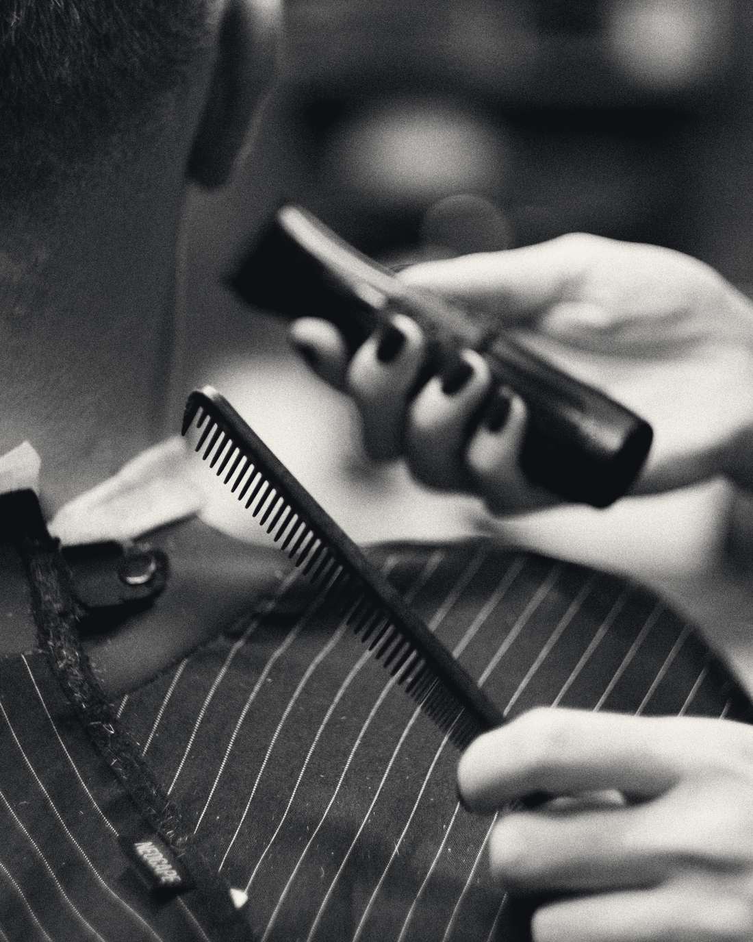 A barber holds a comb and clippers over a client's shoulder, the client in a pinstripe cape