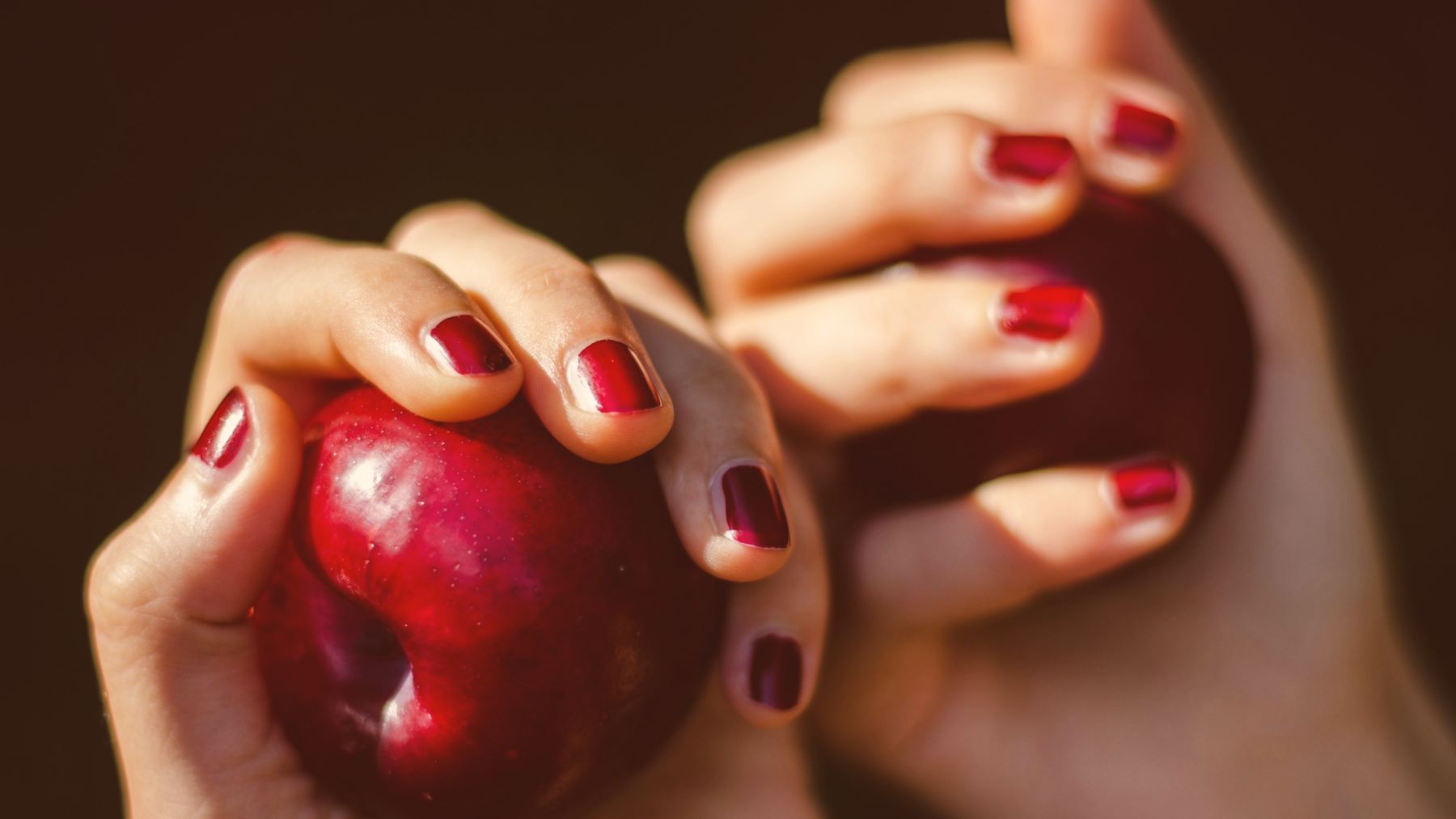 Hands with dark cherry nails holding ripe plums against a dark background