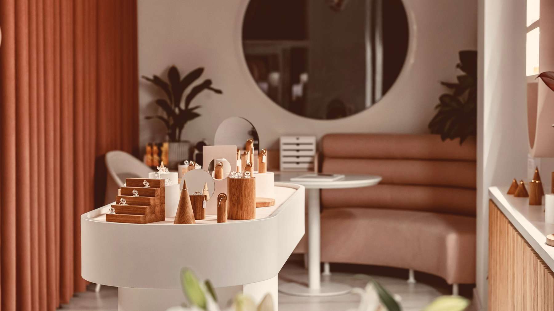 The salon: a curved white reception desk with products, a round mirror and a blush velvet banquette