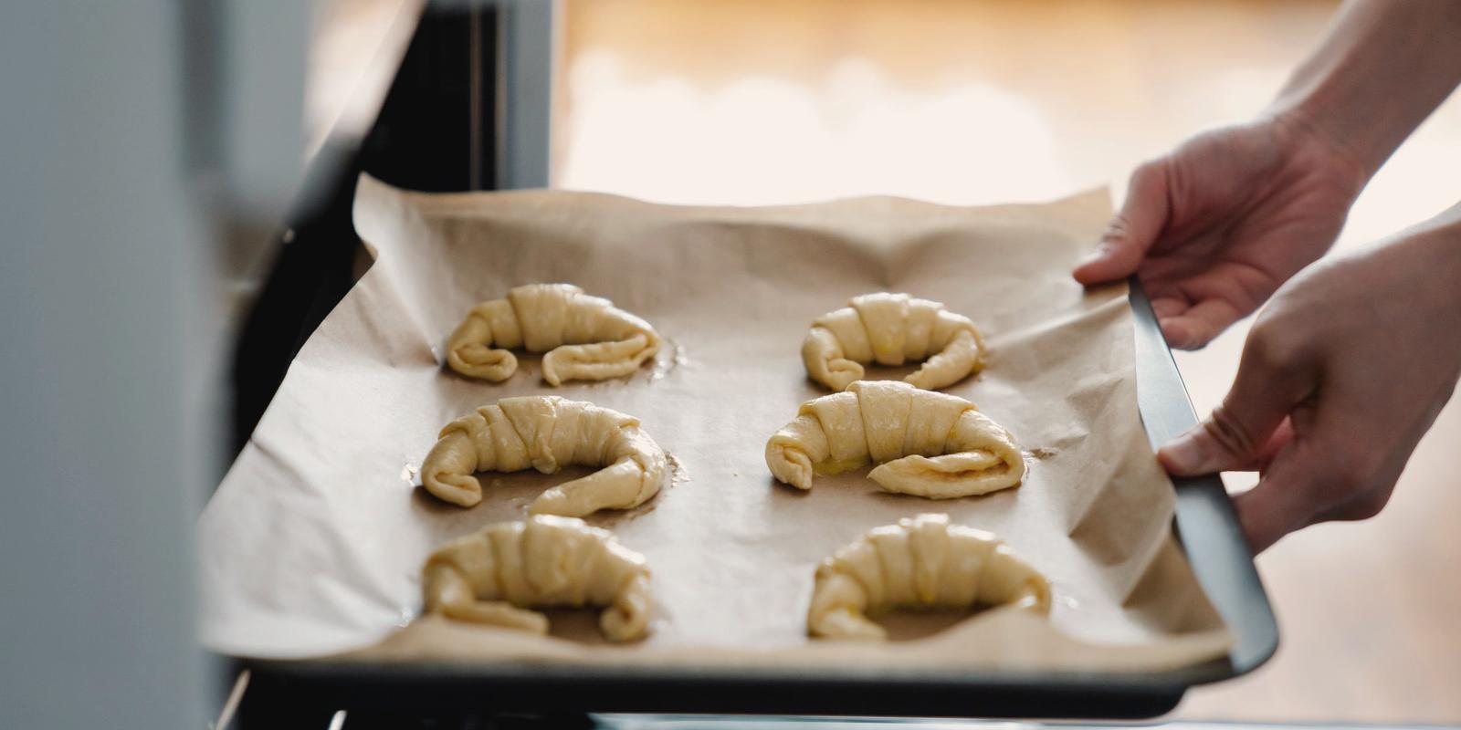 Hands sliding a tray of unbaked croissants into the oven