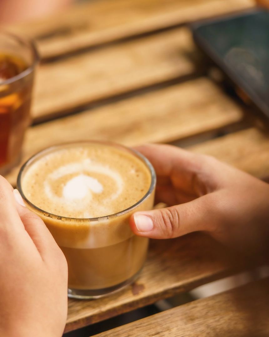 Two people at a wooden table passing a latte and a glass of tea