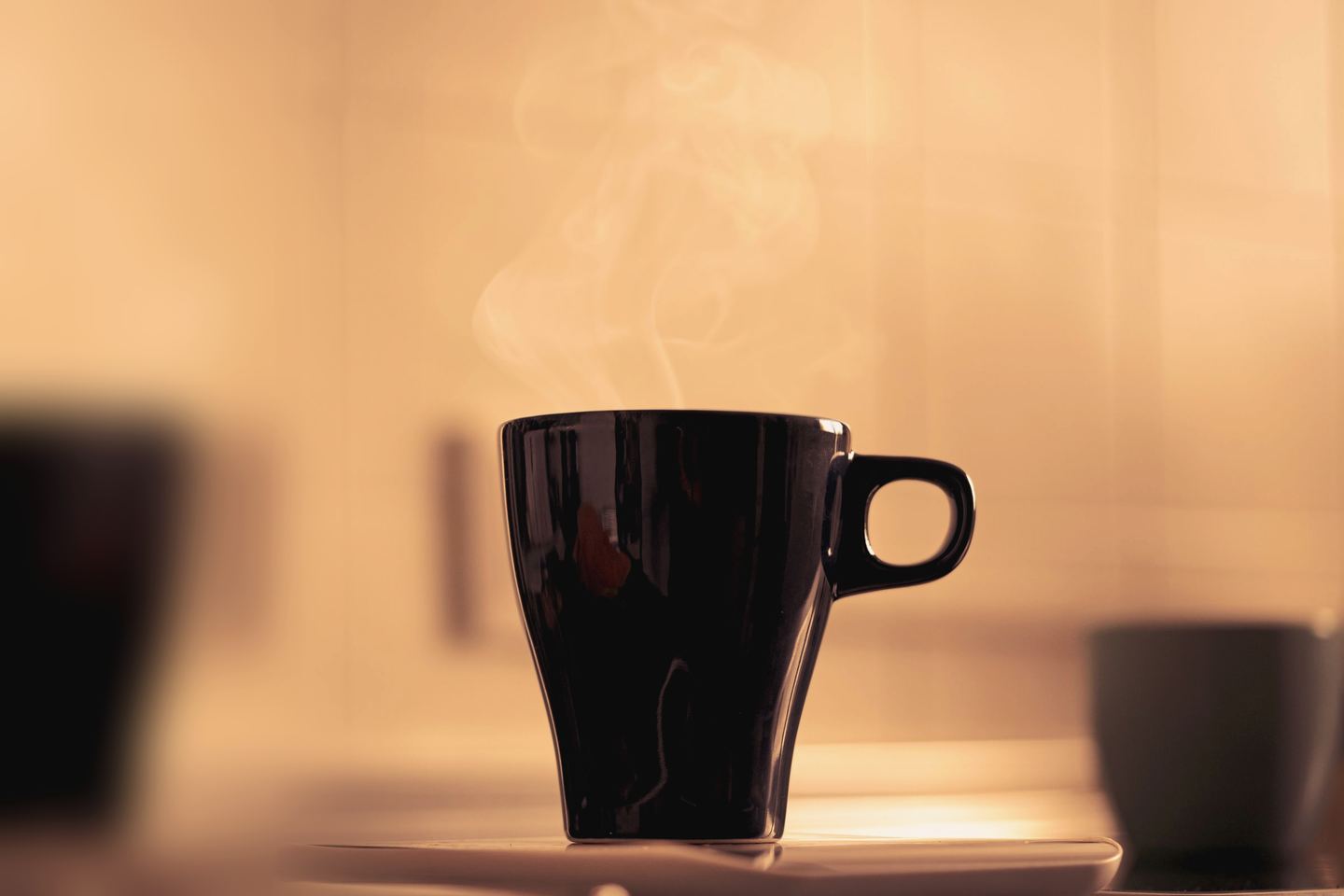 Steam rising from a black mug of coffee in warm early-morning light