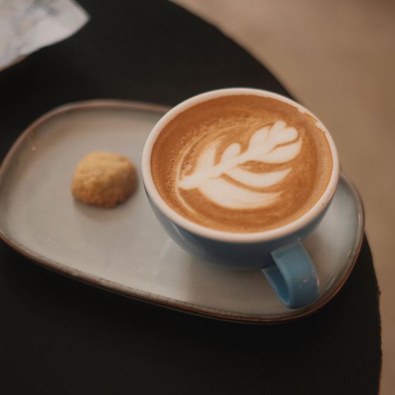 Latte with leaf art in a blue cup, with a biscuit on the saucer