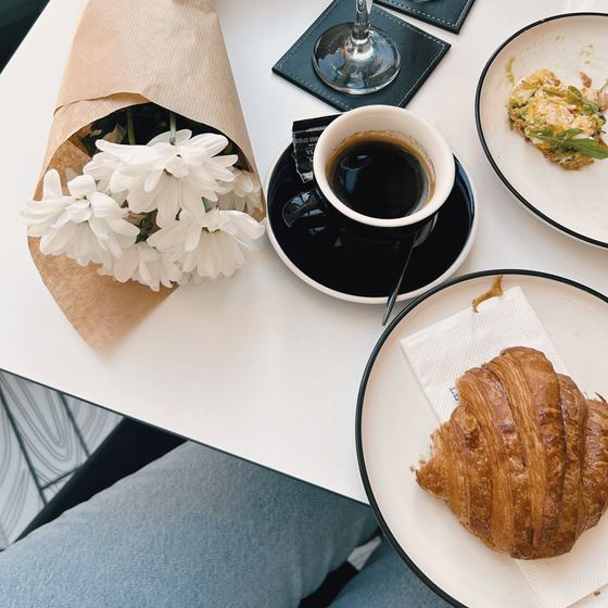 Coffee, a croissant and white flowers on a café table, from above