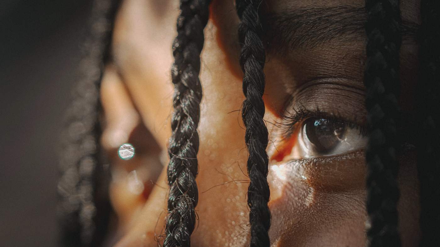 Close-up of a woman with deep brown skin and braided hair, one eye catching the light