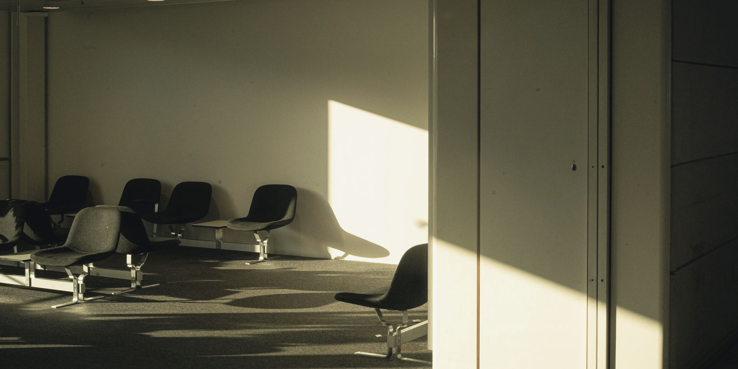 Late sunlight falls across rows of empty chairs in a quiet modern waiting area.