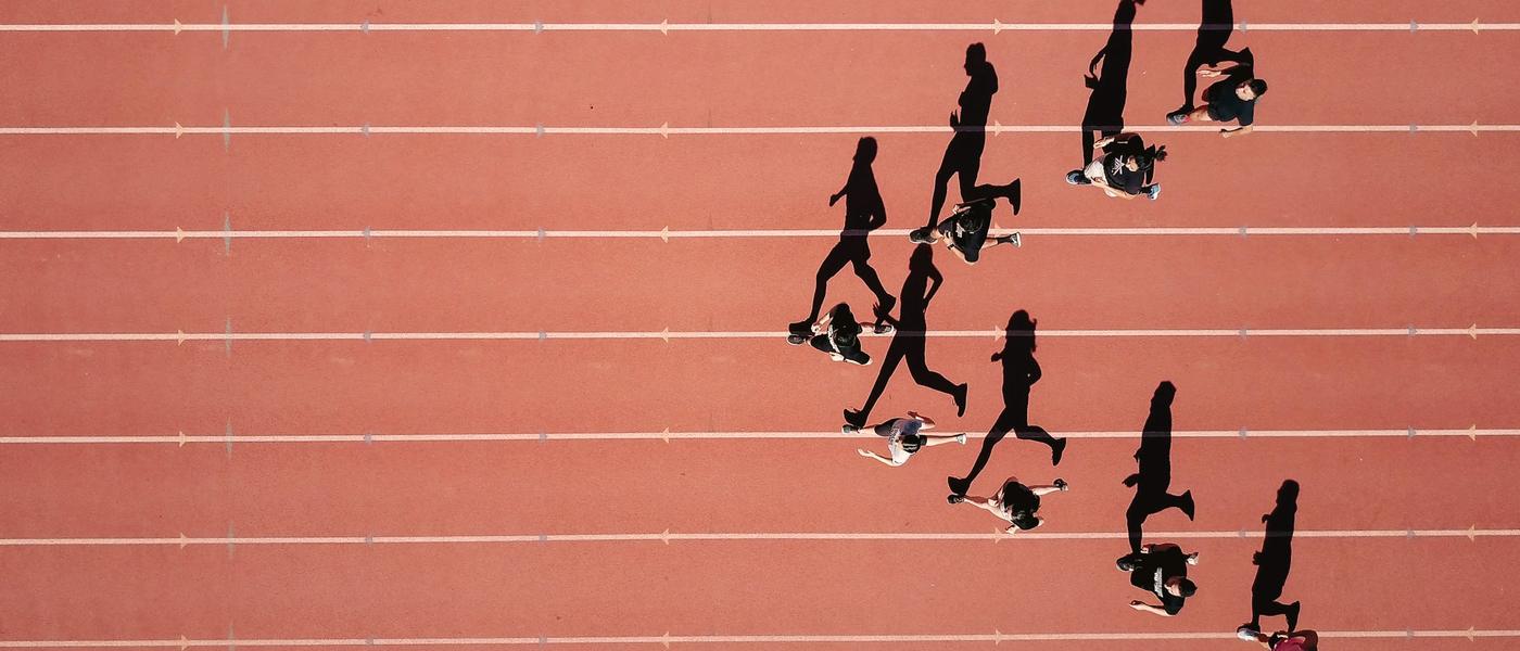Runners on an athletics track seen from above, casting long shadows