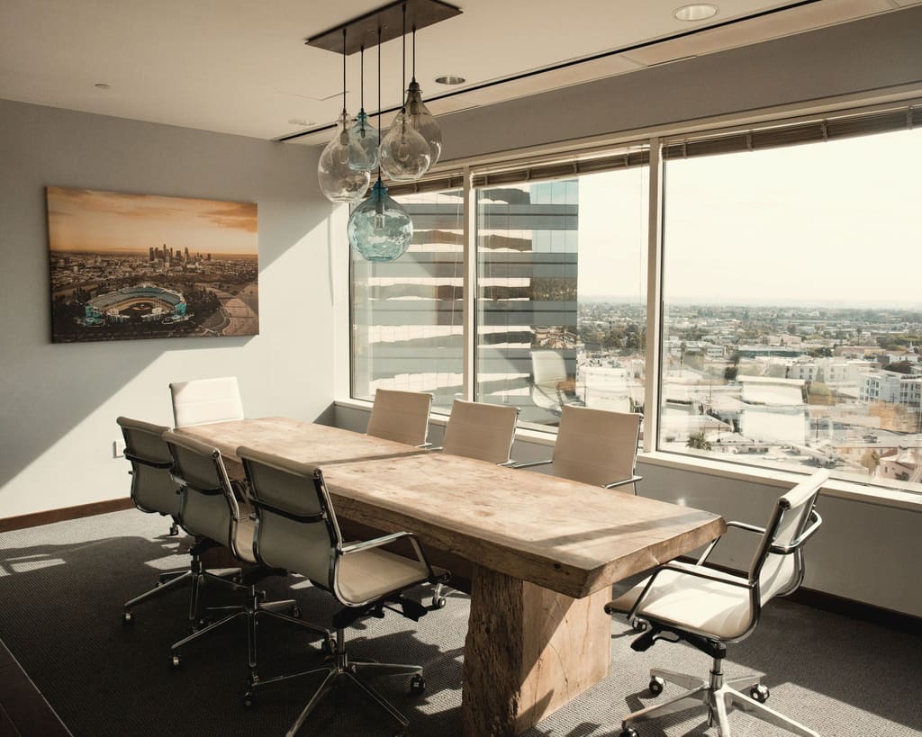 A long timber table with white chairs beside a wall of windows