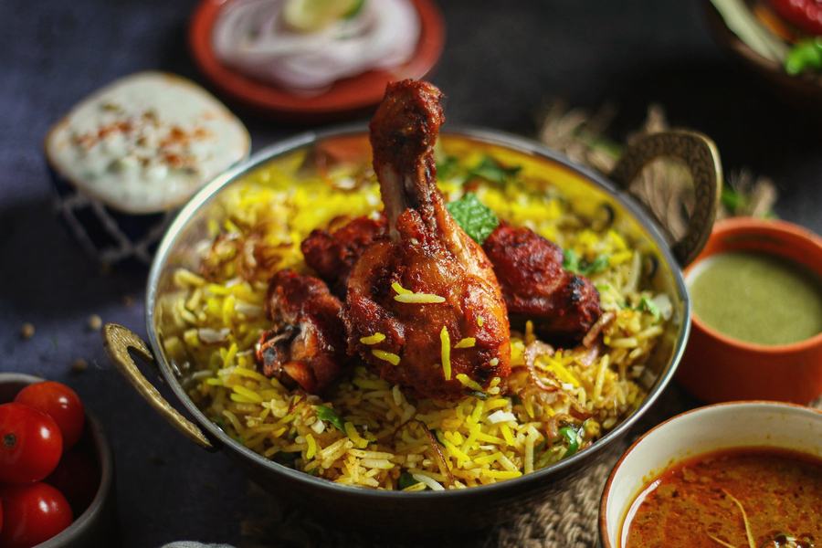Chicken biryani in a handi with raita and salan alongside