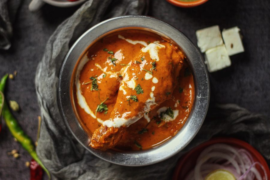 Butter chicken in a hammered steel bowl with sliced onion and green chilli