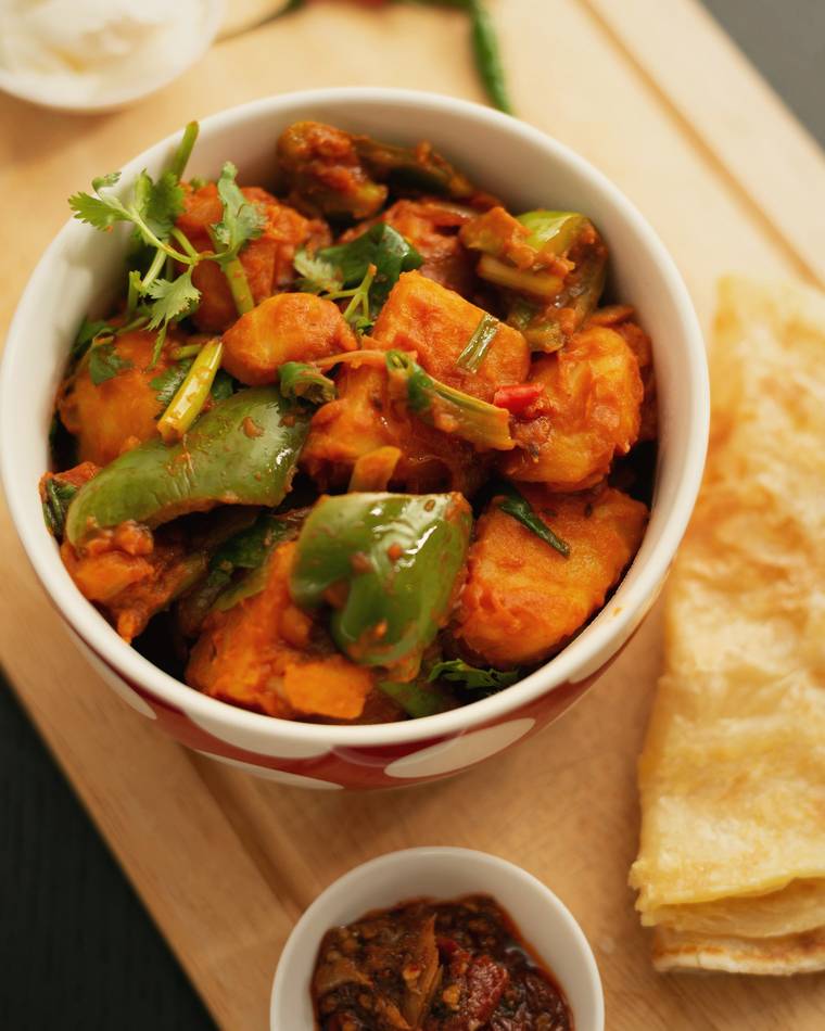 Chilli paneer with peppers in a bowl beside paratha