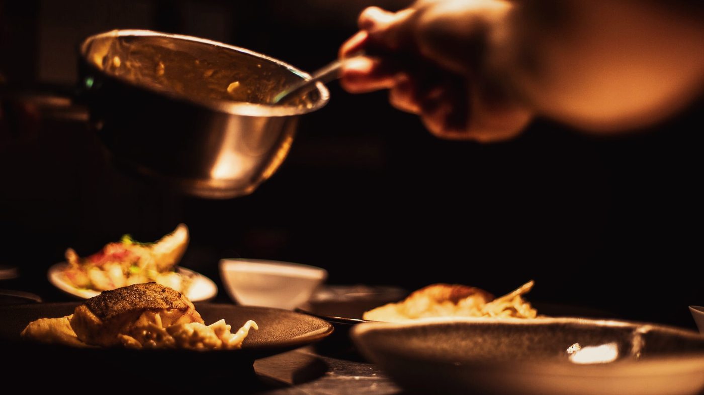 A ladle of curry being served into a bowl in low light