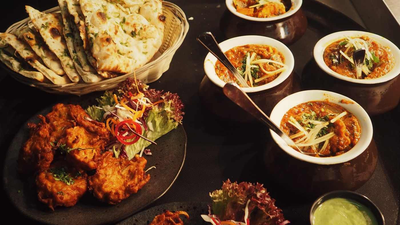 A table of bhajis, naan and small bowls of curry, shared