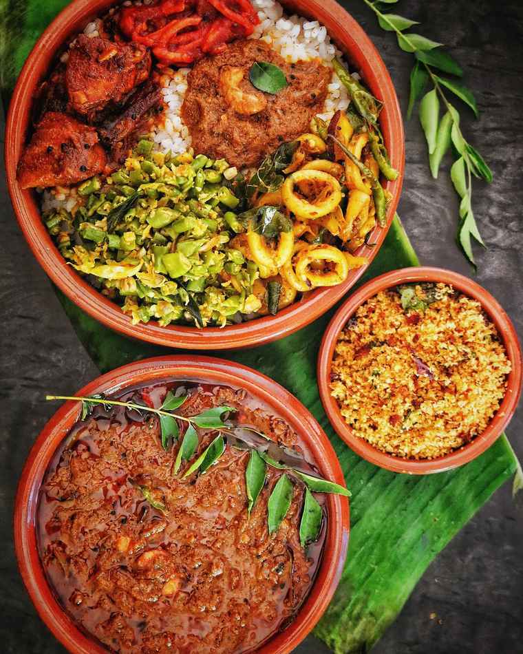 A thali of small curries in clay bowls on a banana leaf