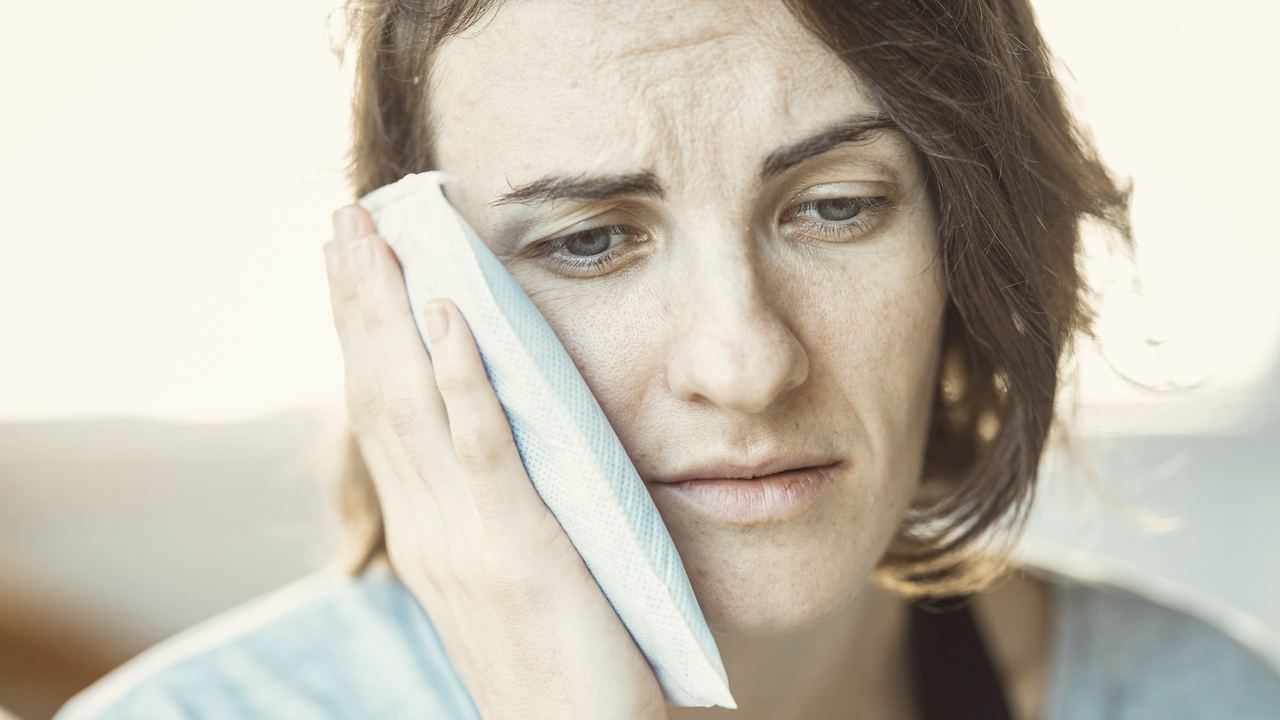 A woman holding an ice pack to her cheek, looking worn out with toothache