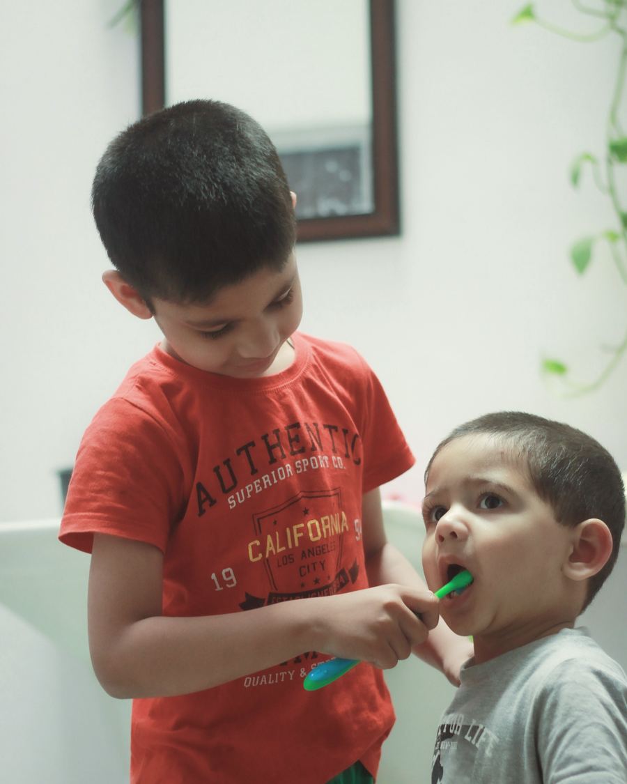An older brother helping his little brother brush his teeth at the sink
