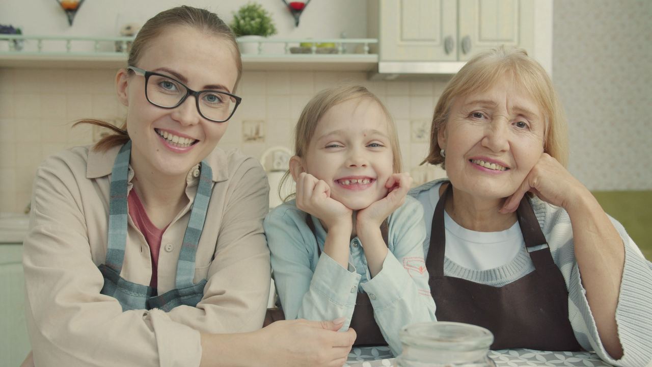 A mum, her daughter and grandmother smiling together at the kitchen table