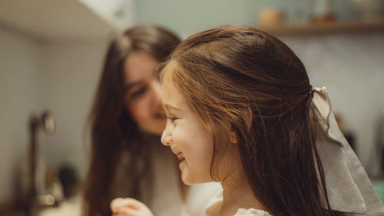 A little girl laughing with her mum at the bathroom basin
