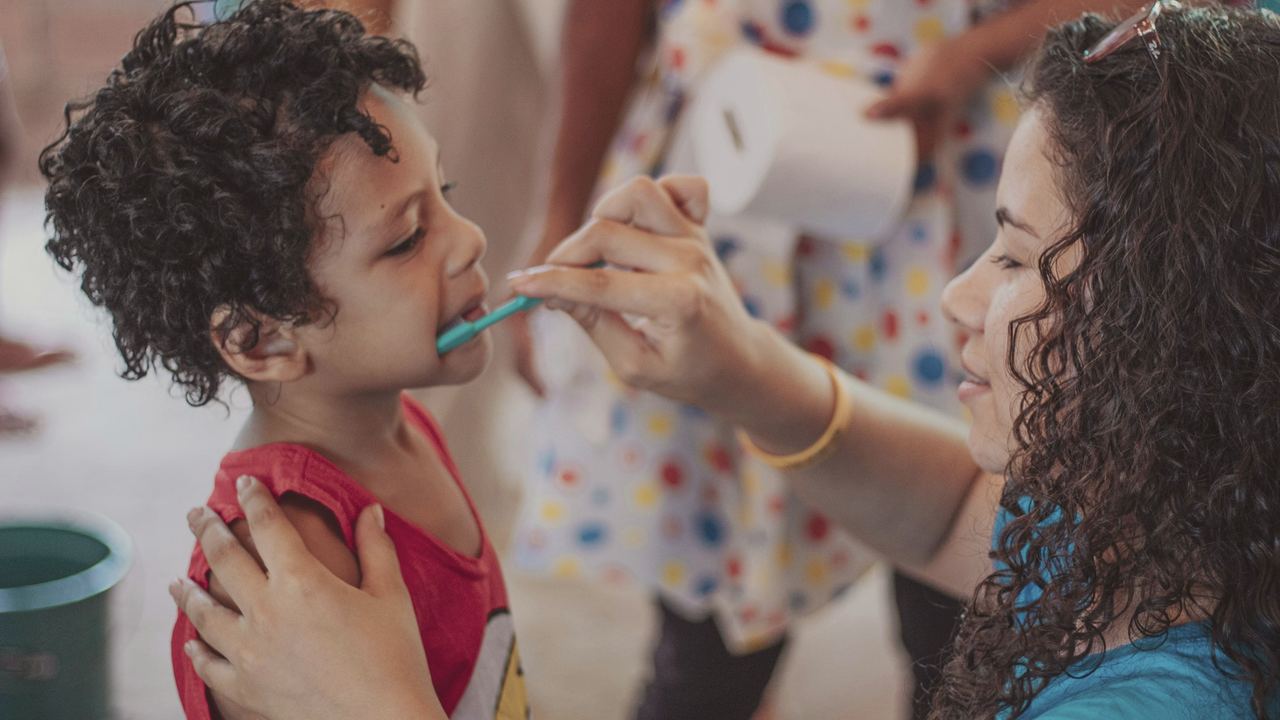 A mum gently brushing her young son's teeth while he holds still and looks up at her