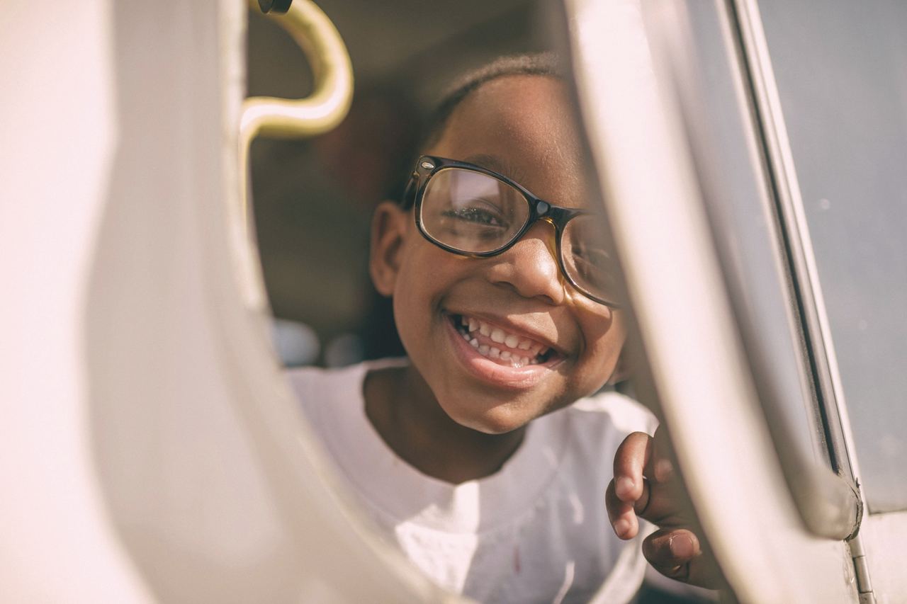 A girl in glasses grinning from the dental chair, peeking round the light