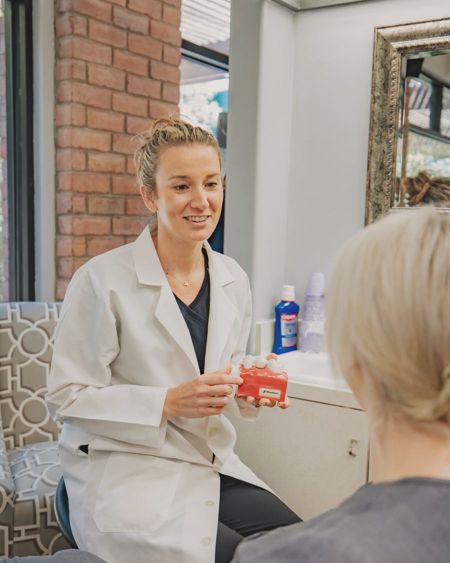 A dentist in a white coat chatting with a patient and showing her a model of teeth