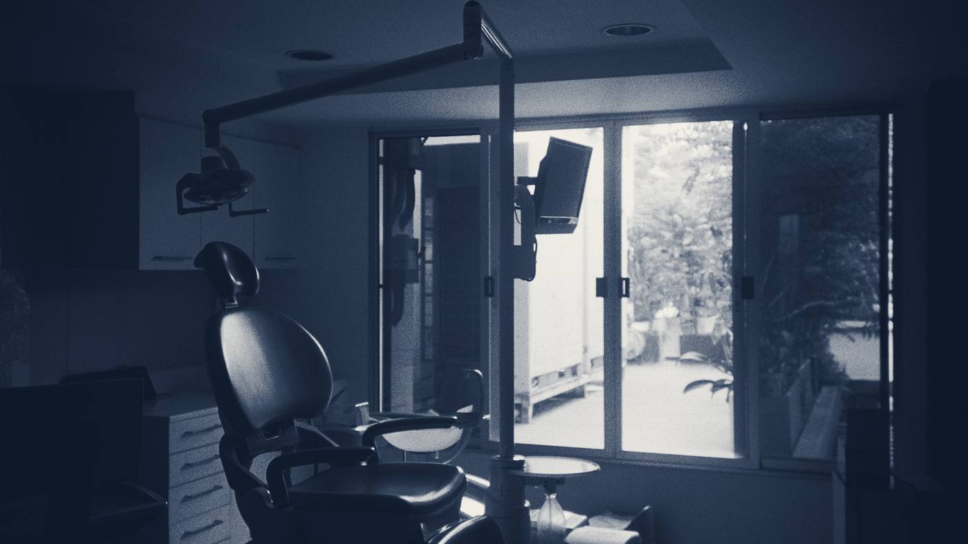 A dental chair in a darkened surgery, silhouetted against a bright window