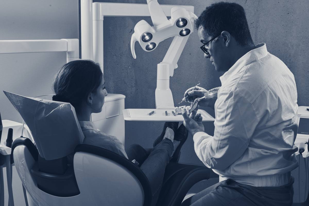 A dentist in a white shirt talks with a patient sitting up in the treatment chair