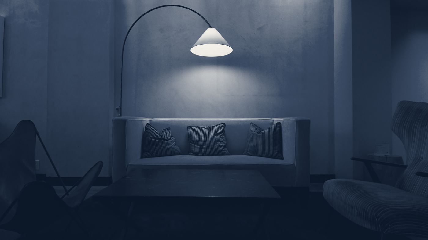 A quiet sitting room lit by one arched floor lamp, with a low sofa and cushions