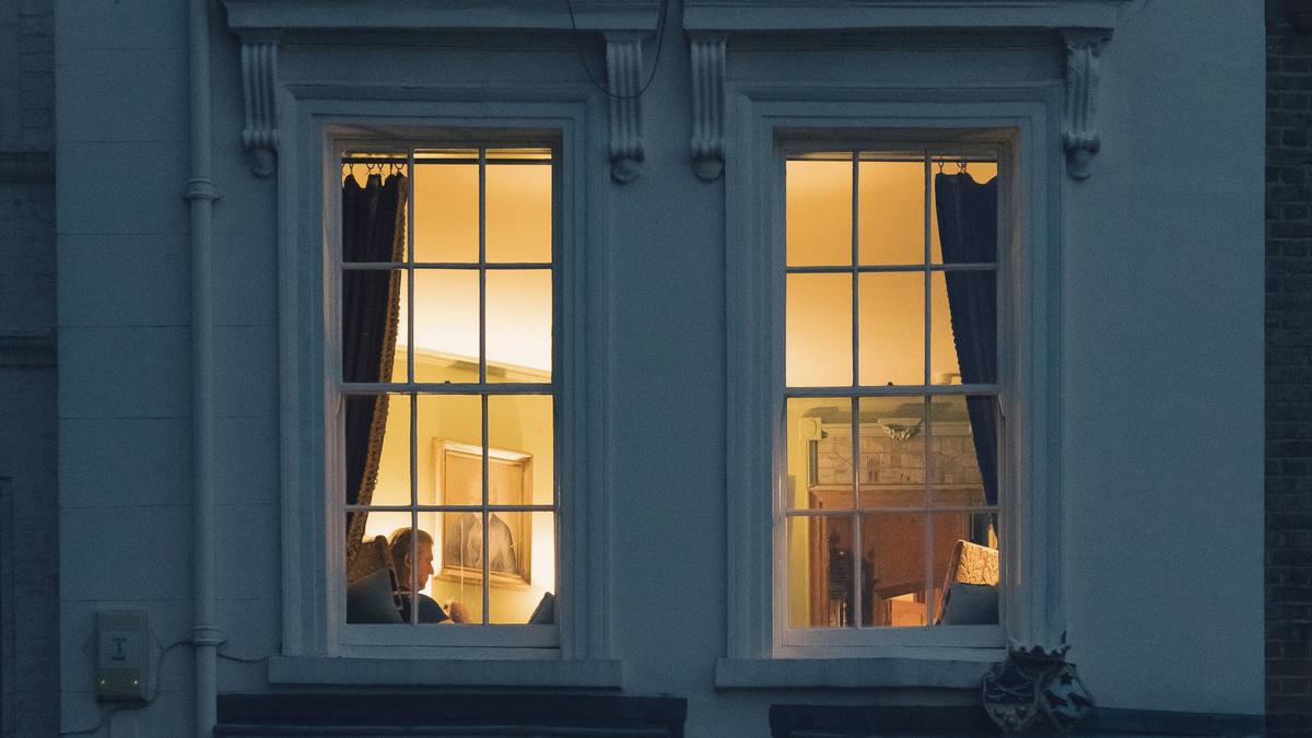 A pale London townhouse at blue hour, its two tall sash windows glowing with warm lamplight