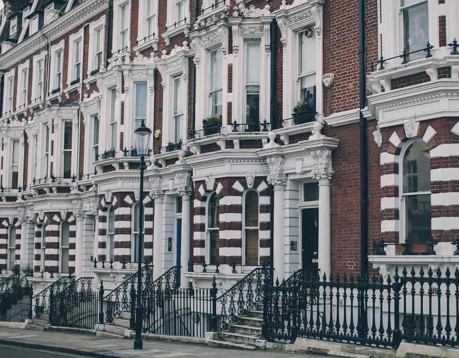 A long terrace of red-brick and white-stucco Victorian houses with bay windows, iron railings and a street lamp