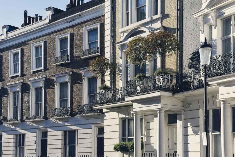 Classic London townhouses with white stucco, black iron balconies, clipped bay trees and a street lamp