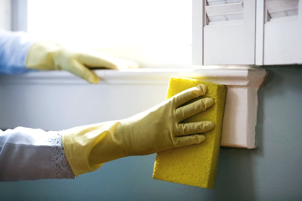 A gloved hand wiping a windowsill with a sponge