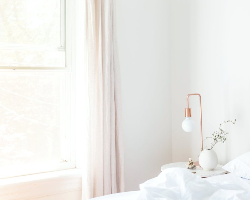 A calm, freshly made bed in a bright white bedroom with the window open