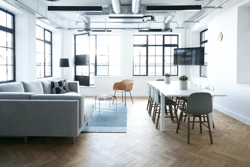 A bright open-plan office with a sofa, dining table and tall windows