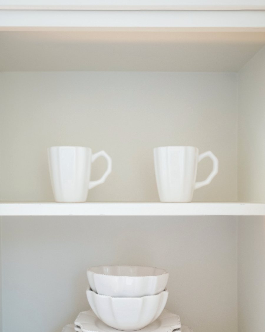 Clean white mugs and bowls neatly stacked on an open shelf
