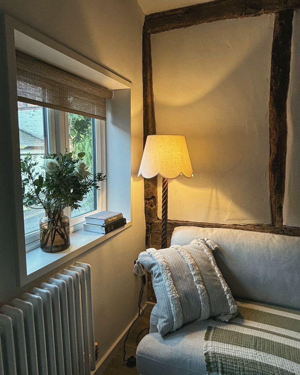 A cottage sitting room with a lamp and a deep window