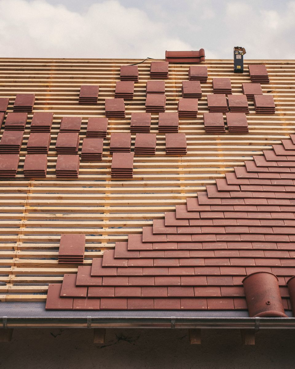 Clay roof tiles being fixed to new battens on a roof under construction